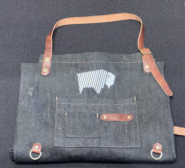 Folded denim apron with pockets and leather straps, ideal for BBQ and cooking.