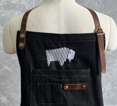 Denim apron displayed on a mannequin with an embroidered bison logo on the chest.