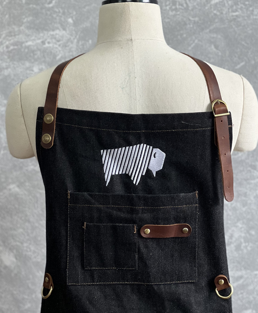 Denim apron displayed on a mannequin with an embroidered bison logo on the chest.