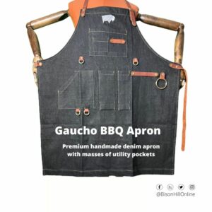 Denim BBQ apron displayed on a mannequin with multiple pockets, leather straps, and a metal ring, titled "Gaucho BBQ Apron."