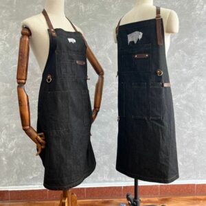 Two denim BBQ aprons with multiple pockets and leather straps displayed on mannequins.