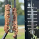 A close-up view of two vertical skewers holding grilled meat, hanging from a stainless steel skewer stand.