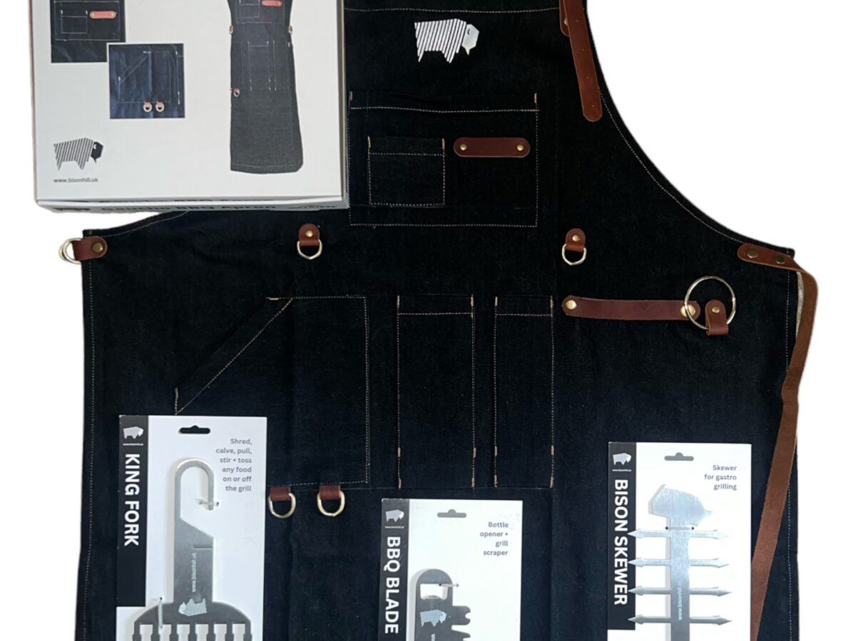 A BBQ gift set including three stainless steel tools: a meat shredder, grill scraper, and skewer, along with a black BBQ apron, all neatly arranged.