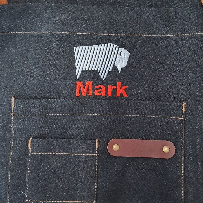 A personalised Bison Hill BBQ apron featuring custom embroidered text in red from a choice of five threads on the denim apron.