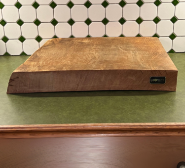 Close-up of Bison Hill BBQ Block product tag on a handmade English Oak cutting board, air-dried for 2 years, in an outdoor setting