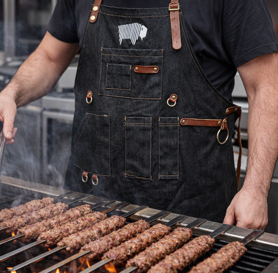 Black leather-strap BBQ apron worn while grilling Turkish-style kebabs over open flames