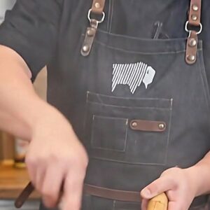 Cook wearing a black BBQ apron with leather straps using a wok over high heat in an outdoor kitchen