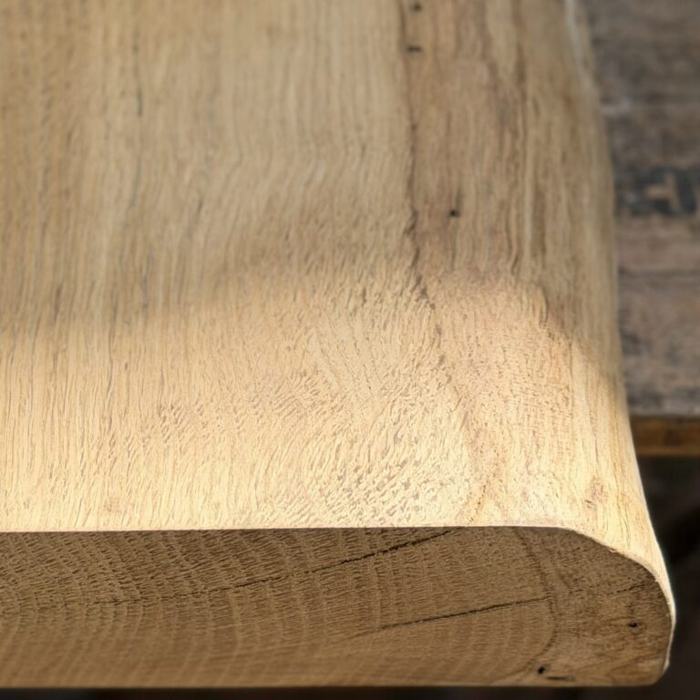 Macro view of the rounded live edge slope on a solid oak chopping board, showing rays and flecks in the wood grain.